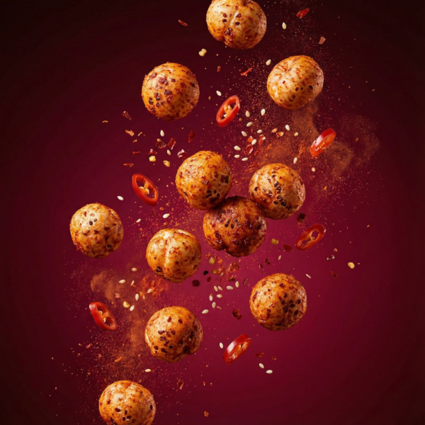 Floating gochujang makhana showing its crunchy texture and deep red spice coating against a soft background